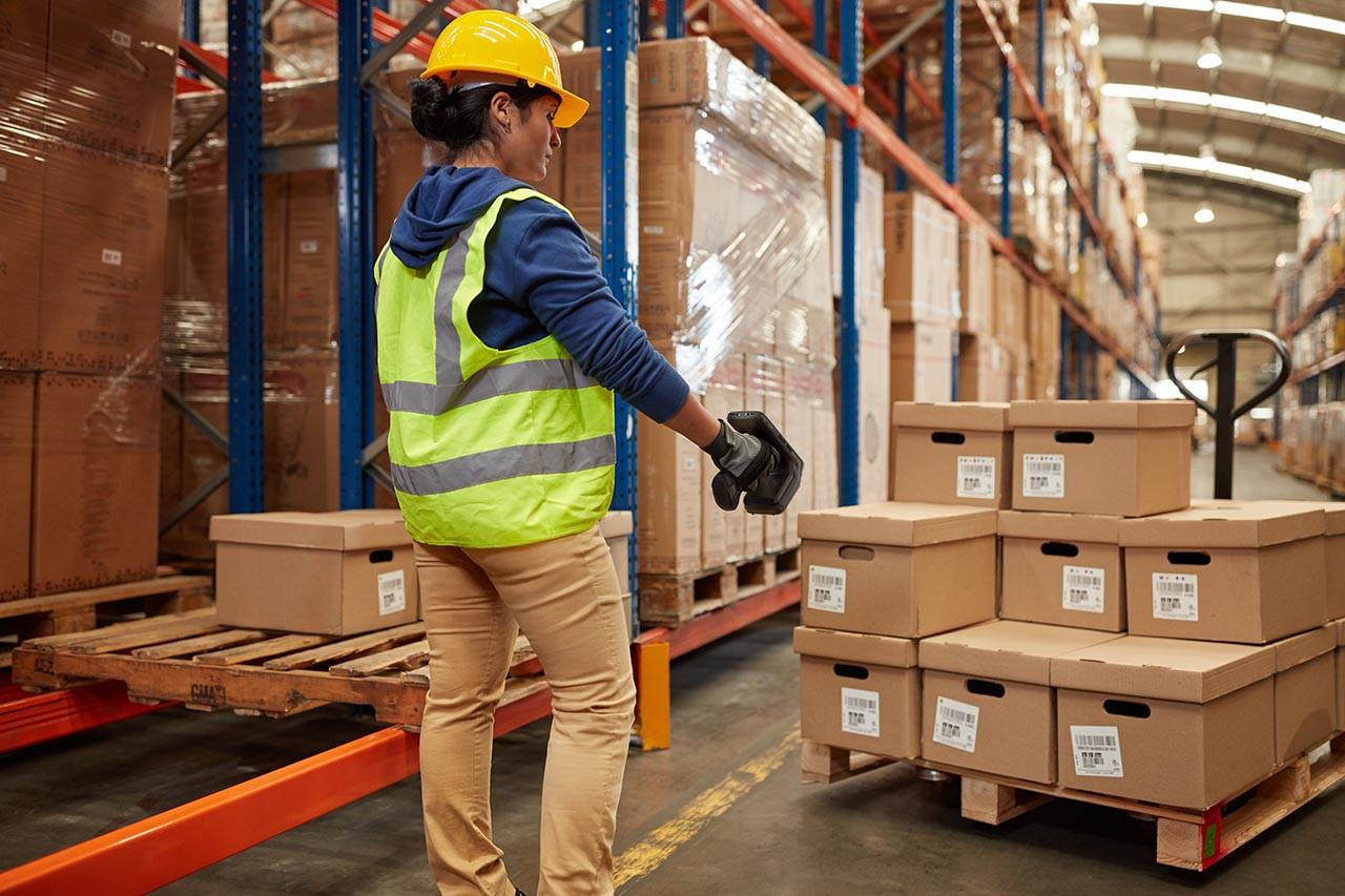 Warehouse employee using a handheld RFID reader to identify multiple tagged cartons during inventory counting.